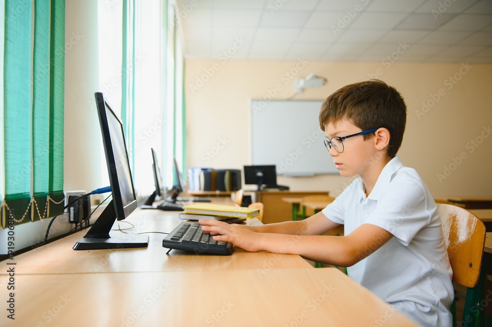 Teenage boy smiling while using computer at desk in classroom Teenage boy smiling while using computer at desk in classroom