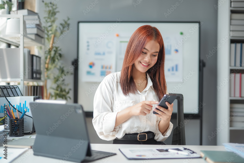 Asian businesswoman is smiling while using her smartphone at her desk in a bright and modern office Asian businesswoman is smiling while using her smartphone at her desk in a bright and modern office