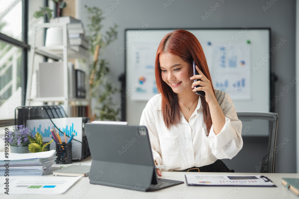 Young asian businesswoman smiling and talking on the phone while working on a digital tablet in the office Young asian businesswoman smiling and talking on the phone while working on a digital tablet in the office