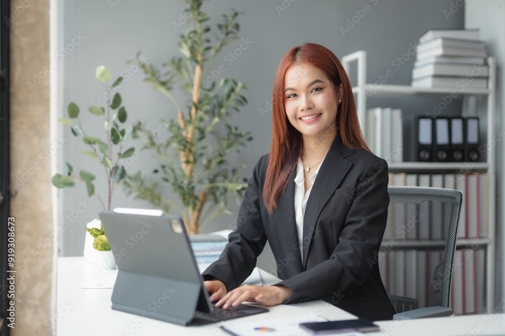 Smiling asian businesswoman working on a tablet computer while sitting at her desk in a modern office Smiling asian businesswoman working on a tablet computer while sitting at her desk in a modern office