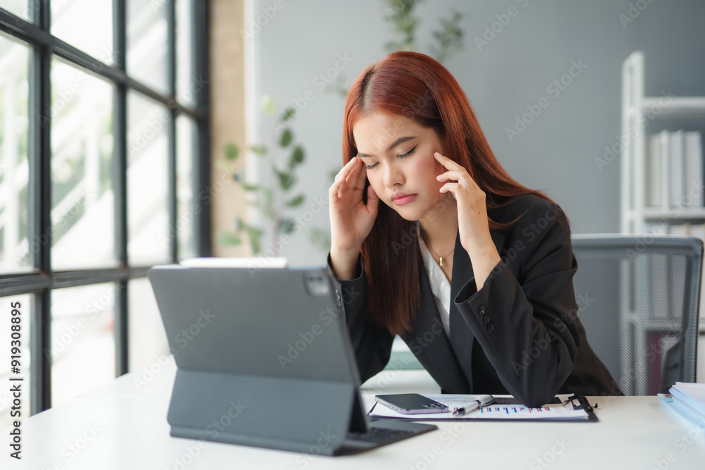 Businesswoman is feeling tired and having a headache while working on a report using a digital tablet in the office Businesswoman is feeling tired and having a headache while working on a report using a digital tablet in the office