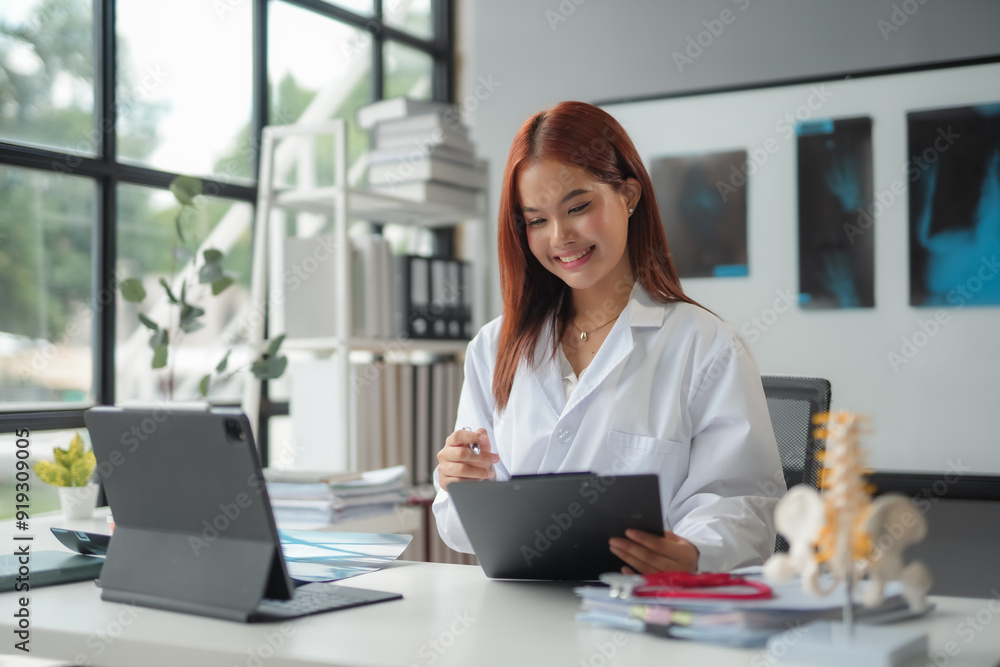 Young doctor is smiling while reviewing medical records on a clipboard at her desk Young doctor is smiling while reviewing medical records on a clipboard at her desk
