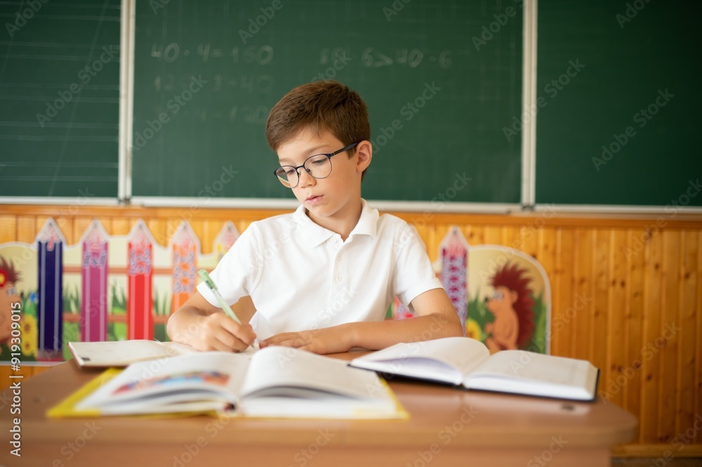Happy schoolboy sitting at desk, classroom Happy schoolboy sitting at desk, classroom