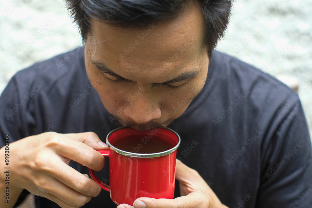 Close up of a man wearing black t shirt sitting on bamboo chair, drinking black coffee on red mug, relax time. Close up of a man wearing black t shirt sitting on bamboo chair, drinking black coffee on red mug, relax time.