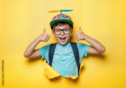 Un garçon écolier sur fond jaune de papier déchiré montre un doigt vers le haut ou un pouce vers le haut, c'est la rentrée scolaire ! photo