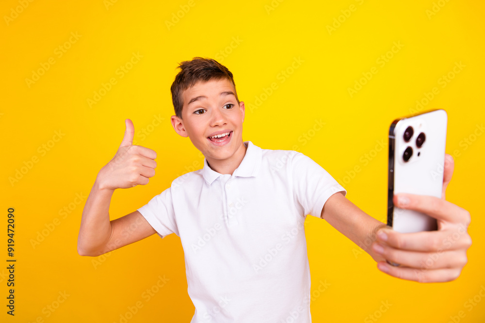 Photo of cheerful positive boy dressed polo t-shirt showing thumb up tacking selfie modern gadget isolated yellow color background Photo of cheerful positive boy dressed polo t-shirt showing thumb up tacking selfie modern gadget isolated yellow color background