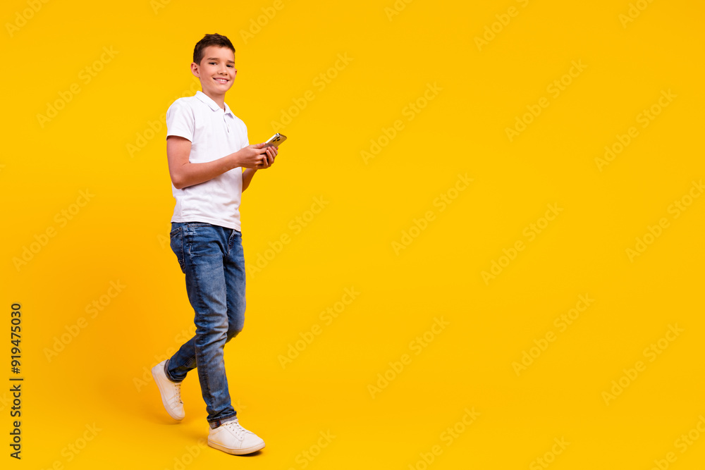 Full length photo of cheerful positive boy dressed polo t-shirt chatting modern gadget emtpy space isolated yellow color background Full length photo of cheerful positive boy dressed polo t-shirt chatting modern gadget emtpy space isolated yellow color background