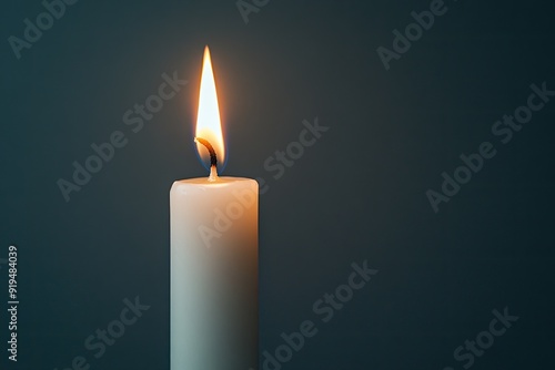 A lit white candle stands against a dark background, casting a warm glow and creating a serene and calming atmosphere.