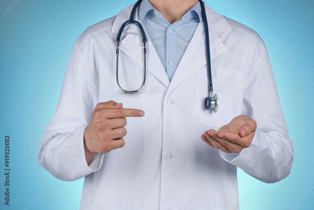 Doctor pointing at something on light blue background, closeup Doctor pointing at something on light blue background, closeup