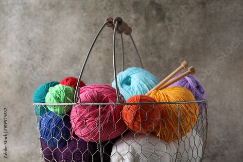 Fotografie Many soft skeins of yarn and knitting needles in metal basket on grey background