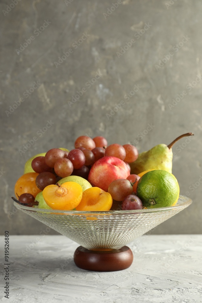 Glass vase with different fresh fruits on gray textured table, space for text Glass vase with different fresh fruits on gray textured table, space for text