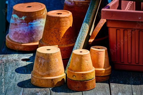 Red clay planter pots lay stacked on an old wooden table outside in the weather at a local Antique Shop in Upstate NY.  Used clay pots for sale.