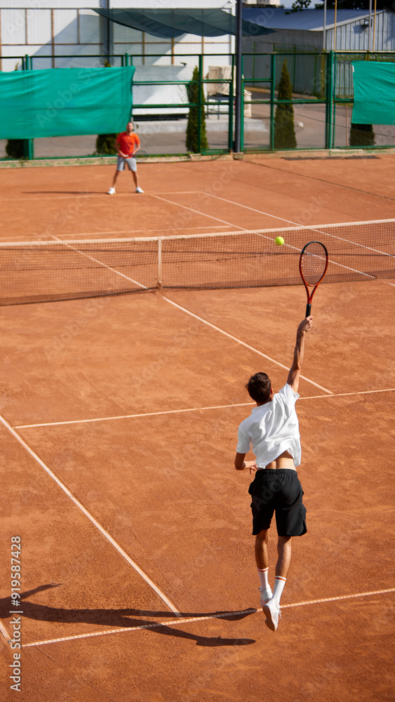 Vertical image of two men, tennis players in motion on clay court, showing competitive game and readiness to make move. Concept of sport, competition, active and healthy lifestyle Vertical image of two men, tennis players in motion on clay court, showing competitive game and readiness to make move. Concept of sport, competition, active and healthy lifestyle