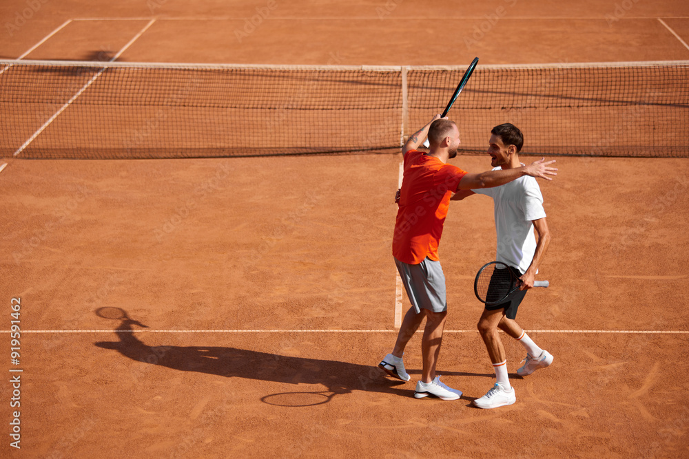 Fototapeta premium Happy positive men, friends, tennis players embracing each other after good intense game on outdoor clay court. Mutual respect. Concept of sport, competition, active and healthy lifestyle