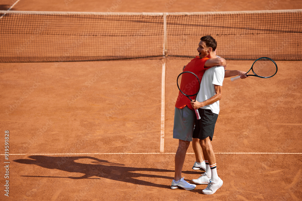 Obraz premium Happy positive men, friends, tennis players embracing each other after good intense game on outdoor clay court. Respectful moment. Concept of sport, competition, active and healthy lifestyle