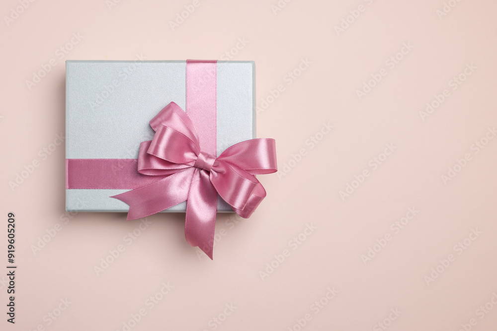Beautiful gift box with pink bow on beige background, top view. Space for text Beautiful gift box with pink bow on beige background, top view. Space for text