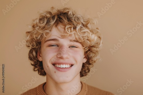 portrait of 20 year old happy caucasian young man or teenage with blonde curly hair on beige background, student photo