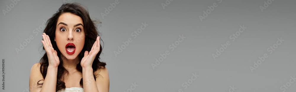 Shocked woman poses gracefully on gray backdrop. Shocked woman poses gracefully on gray backdrop.