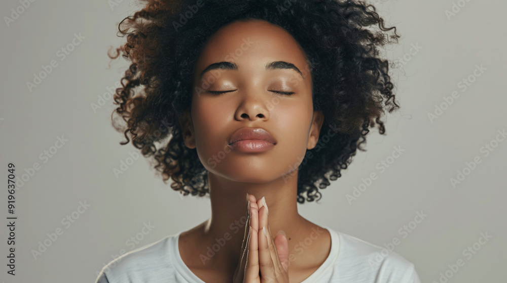 Young woman with curly hair is closing her eyes and clasping her hands in prayer Young woman with curly hair is closing her eyes and clasping her hands in prayer