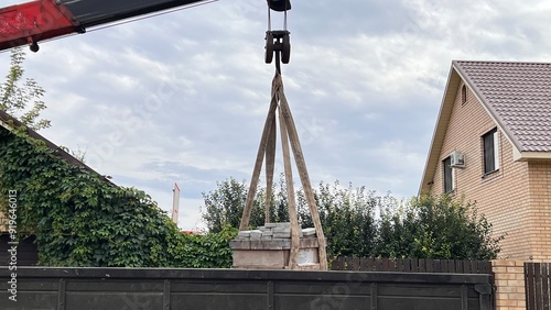 A loader manipulator unloads paving slabs by means of a crane at a house in a rural area. paving stones, concrete paving slabs on palettas photo