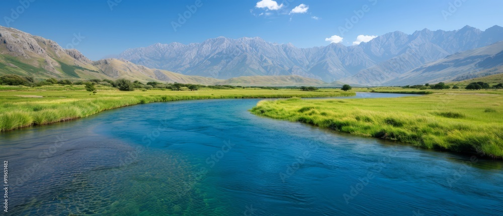 A river runs through two lush green fields, with a mountain range in the background A river runs through two lush green fields, with a mountain range in the background