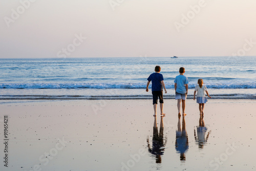 Three children, happy siblings on ocean beach at sunset. happy family, two school boys and one little preschool girl. Brothers and sister having fun, Spain, Costa del Sol photo