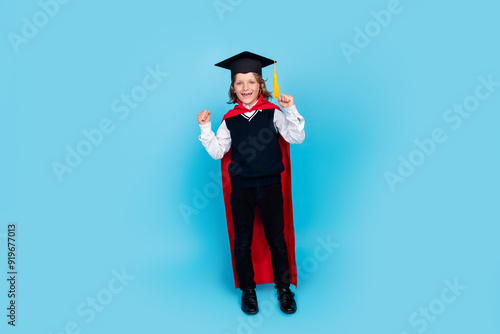 Full size photo of small schoolkid boy wear uniform mortarboard raise fists isolated on blue color background