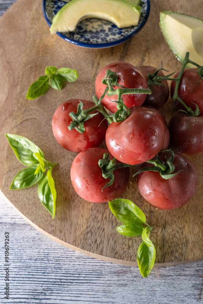 Fresh dark red vine tomatoes on a wooden board with basil leaves close up Fresh dark red vine tomatoes on a wooden board with basil leaves close up