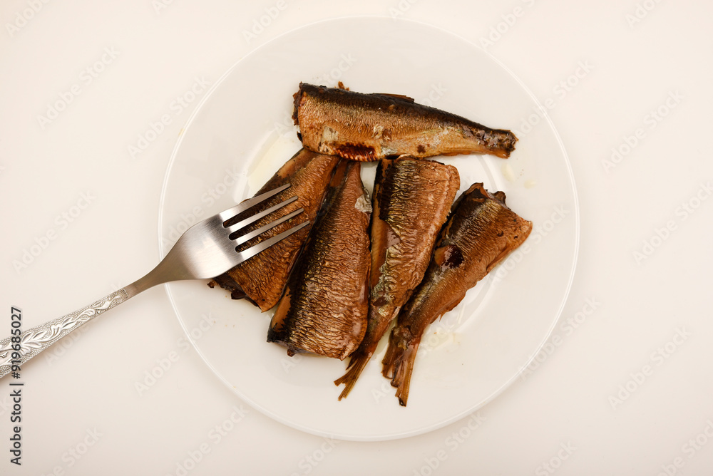 Sprats on a white plate with a fork. Canned fish in oil. Fish appetizer. Sprats on a white plate with a fork. Canned fish in oil. Fish appetizer.