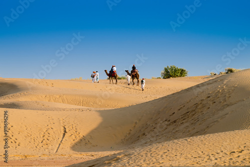 Tourists riding camels, Camelus dromedarius, at sand dunes of Thar desert. Camel riding is a favourite activity amongst all tourists visiting here,