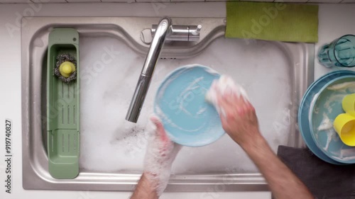 Bubbles rise as a man scrubs dirty dishes in a bright kitchen sink, soaking in the warmth of the afternoon sun.