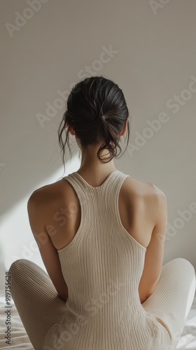 A tranquil moment of a woman in a beige ribbed outfit, seated indoors in soft morning light