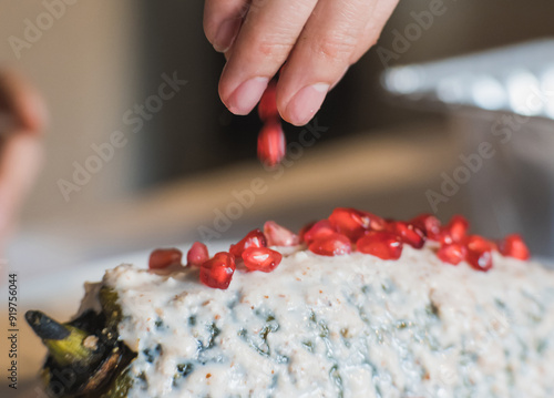 Fotografie Preparation of the famous chiles en Nogada, traditional Mexican food in the month of September, stuffed chile being covered by the nogada which is a cream with walnut and hand adding pomegranate