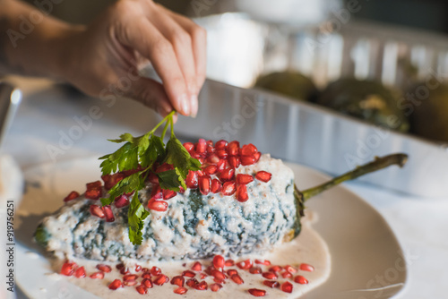 Obraz na plátně Preparation of the famous chiles en Nogada, traditional Mexican food in the month of September, stuffed chile being covered by the nogada which is a cream with walnut and hand adding parsley