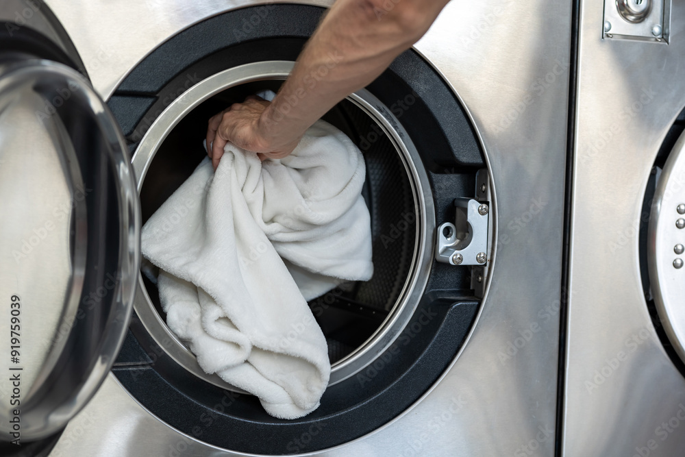 Unknown man doing household chores loading washing machine at public laundry Unknown man doing household chores loading washing machine at public laundry