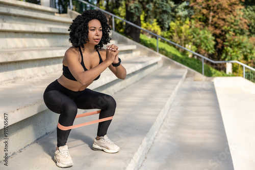 Brunette woman in black top exercising with a power band and doing squats