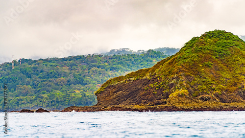 Coastal view of a rocky hillside covered in greenery with a dense forest and cloudy sky in the background, near the Pacific coast. High-quality photo. Uvita Puntarenas Province Costa Rica photo