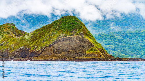 Coastal view of a rocky hillside covered in greenery with a dense forest and cloudy sky in the background, near the Pacific coast. High-quality photo. Uvita Puntarenas Province Costa Rica photo