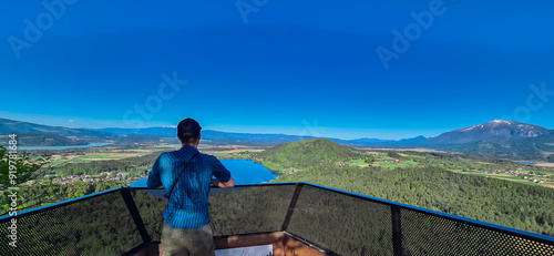 Man at Kitzelberg with aerial view of lake Klopein nestled amidst lush green forest in Carinthia, Austria. Crystal-clear water reflects vibrant blue sky. Rolling hills and mountains in Austrian Alps photo