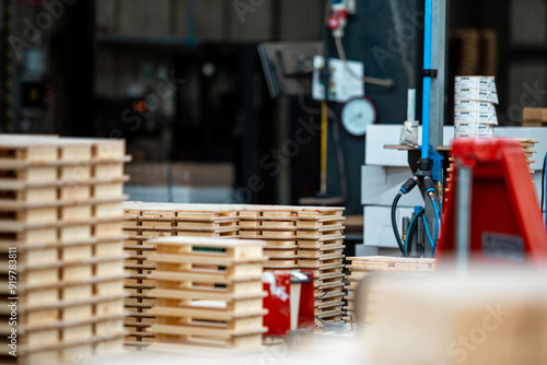 Industrial woodworking facility with stacks of wooden planks and pallets organized for processing, under bright industrial lighting, showcasing a busy and organized work environment photo