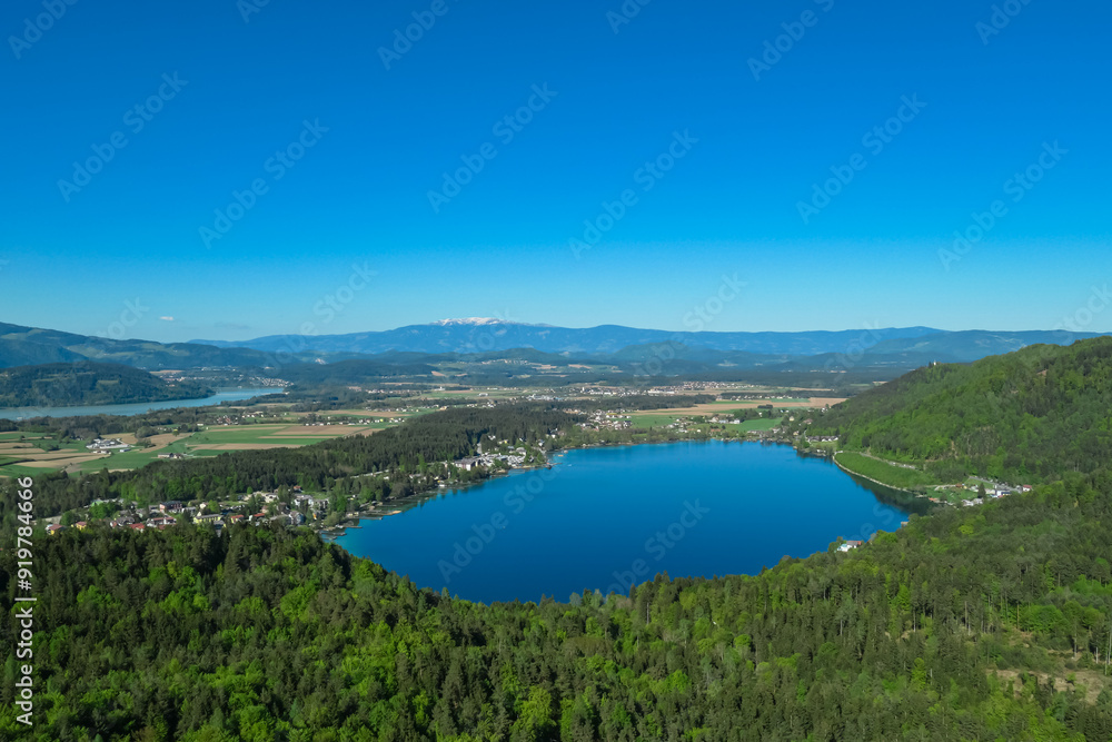 Breathtaking aerial view of a tranquil lake Klopein nestled amidst lush green forest in Carinthia, Austria. Crystal-clear water reflects vibrant blue sky. Rolling hills and mountains in Austrian Alps Breathtaking aerial view of a tranquil lake Klopein nestled amidst lush green forest in Carinthia, Austria. Crystal-clear water reflects vibrant blue sky. Rolling hills and mountains in Austrian Alps