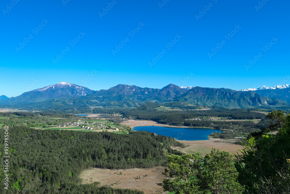 Breathtaking aerial view of a tranquil lake Turnersee nestled amidst lush green forest and Karawanks mountain range in Carinthia, Austria. Crystal-clear water reflects vibrant blue sky. Austrian Alps Breathtaking aerial view of a tranquil lake Turnersee nestled amidst lush green forest and Karawanks mountain range in Carinthia, Austria. Crystal-clear water reflects vibrant blue sky. Austrian Alps
