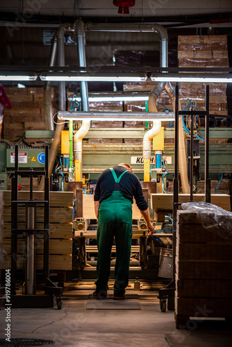 worker operates a computerized machine in a woodworking factory, processing large wooden beams in an industrial setting photo