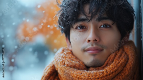 Portrait of a Young Asian Man in a Cozy Scarf with Snowflakes on Hair, Standing Outdoors on a Snowy Day with Soft Bokeh Background