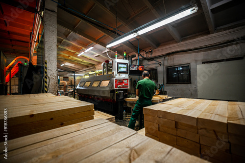 A worker operates a computerized machine in a woodworking factory, processing large wooden beams in an industrial setting photo