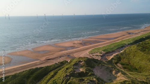 Aerial orbit over grassy sand dunes overlooking wind farm offshore on Scotlands North East coast. 