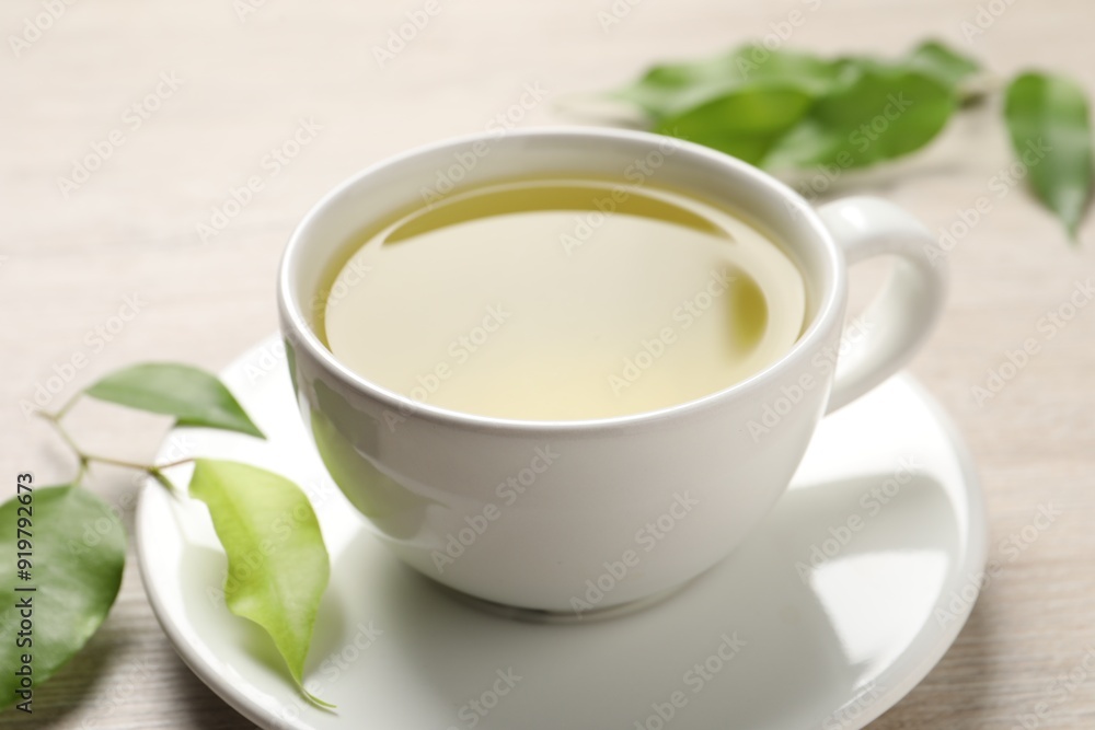 Refreshing green tea in cup and leaves on wooden table, closeup Refreshing green tea in cup and leaves on wooden table, closeup