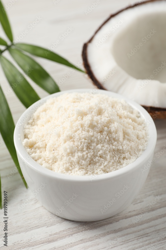 Fresh coconut flour in bowl, nut and palm leaf on white wooden table Fresh coconut flour in bowl, nut and palm leaf on white wooden table
