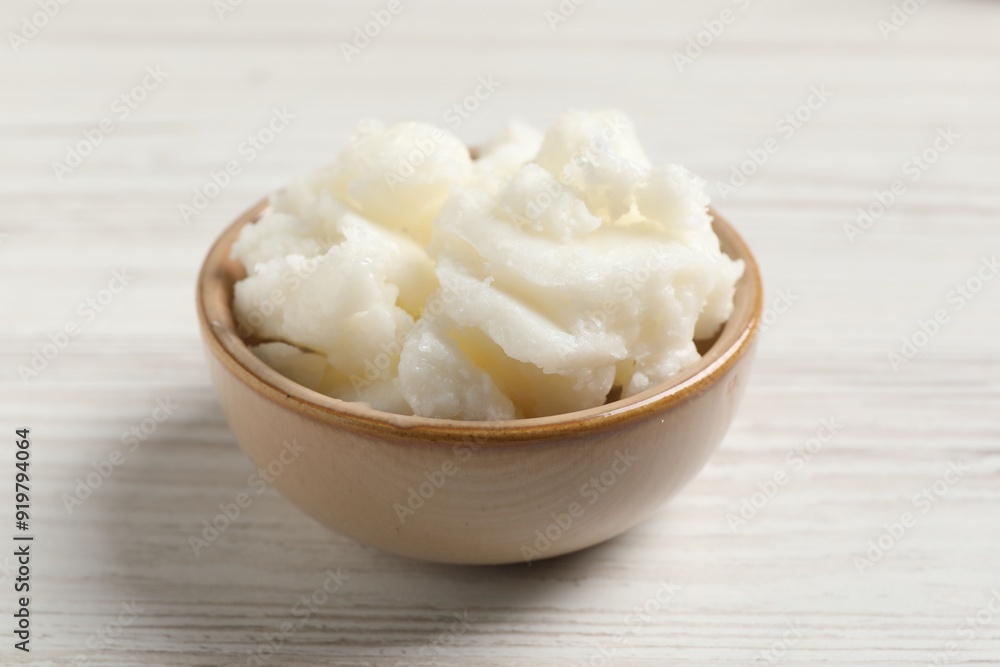 Shea butter in bowl on white wooden table, closeup