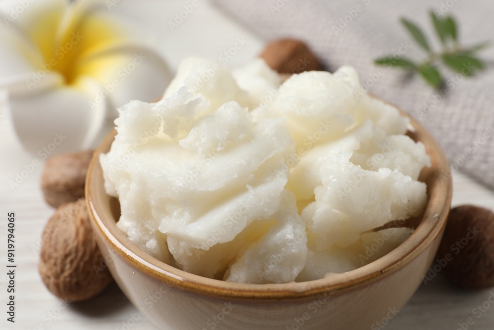 Shea butter in bowl, flower and nuts on white wooden table, closeup Shea butter in bowl, flower and nuts on white wooden table, closeup